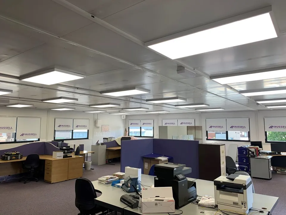 Office desks and workstations arranged beneath ceiling lighting