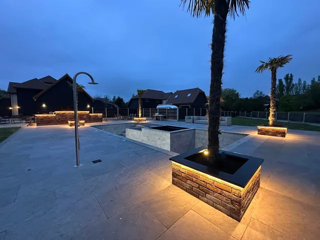 Warm lighting around raised garden planters and a pool terrace